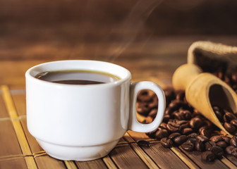 cup of black coffee and grains of coffee in a bag on a wooden table