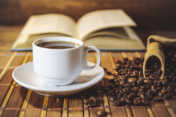 A cup of black coffee on the background of an open book. on a wooden table