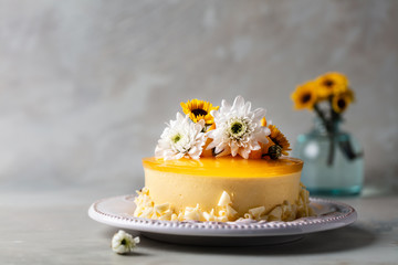 Glazed Mango cheesecake with flowers and fresh mango pieces on grey background , horizontal composition