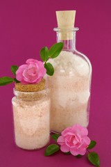 bath salt set with rose extract. sea salt in  bottles and fresh pink rose flowers on bright fuchsia background.Body cosmetics with rose extract
