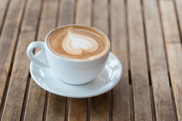 A cup of hot latte, cappuccino or espresso coffee with milk  foam on a  rustic table. White coffee mug with heart shape latte art on wood background.Copy space for your text.