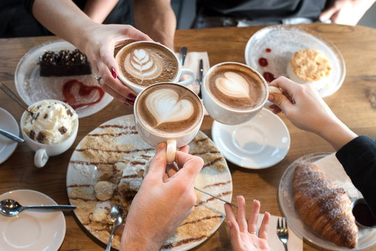 Friends with desserts and coffee, close up.Happy couple sitting around the table. Hands holding cups, happy festive moment, luxury celebration concept.