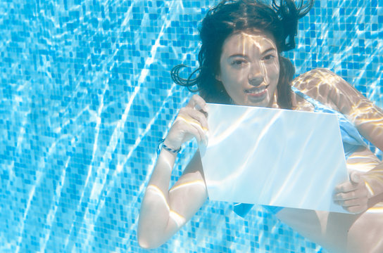 Beautiful young girl holding white blank board in swimming pool under water, fitness and fun on family vacation
