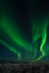 Beautiful stripes of the northern lights, aurora in the night sky above the snow covered hills.