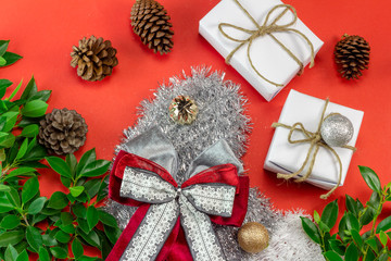 White Christmas gift box on red background decorated with green leaves and pine cone