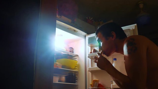 man eats hunger and gluttony from the refrigerator at night. man looks into the fridge at night. gluttony overweight overeating lifestyle concept