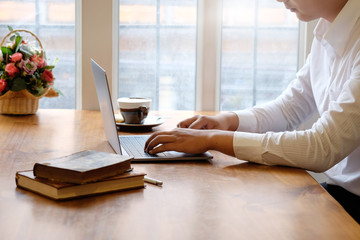 Cropped Man using laptop computer and books with coffee on office desk.