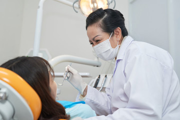 Fototapeta na wymiar Smiling mature Asian dentist examining teeth of teenage girl