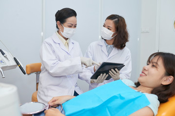 Dentist and nurse discussing jaw x-ray of teenage girl on table computer