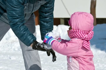 Baby toddler hands with colorful textile gloves and black leather glove of father hand playing with snow. Shallow depth of focus. Winter concept, family games outdoor.