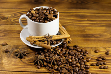 Coffee beans in white cup, cinnamon sticks and star anise on wooden table