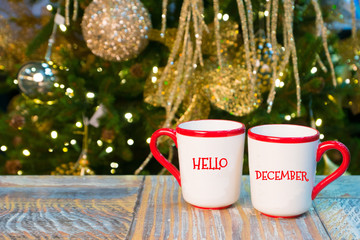 Obraz na płótnie Canvas cups with Hello December greetings on rustic table near xmas decorated tree