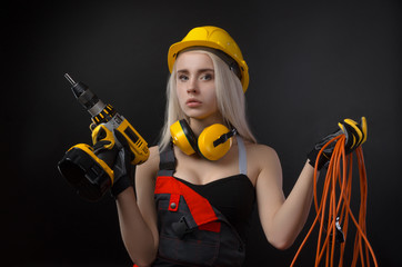 girl in construction clothes and protective equipment posing with a screwdriver
