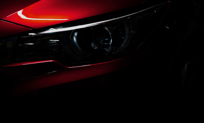 Closeup headlight of shiny red luxury SUV compact car. Elegant electric car technology and business concept. Hybrid auto and automotive concept. Car parked in showroom or motor show. Car dealership.