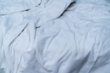 White linen blanket in hotel bedroom. Close up detail of messy white blanket after waking up in morning. Comfortable bed with soft white duvet. Sleep tight with good quality bedding household concept.