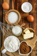 Ingredients for chocolate dough - flour, cocoa, sugar, eggs, butter, milk, baking powder on the wooden rustic table, top view.