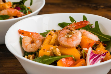 Light fruit salad with fried prawns, persimmon, arugula and walnuts in white bowl on wooden rustic table, close-up