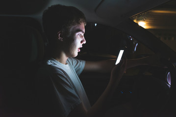 Teenager sitting in his parked car while using his smartphone. He is typing up a message before he...