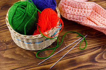 Wicker basket with colorful knitting yarns, knitting needles and knitted scarf on wooden table
