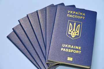 Ukraine passports with golden trident emblem and letters on blue blurred background. Stack of id ukranian documents with selective focus.