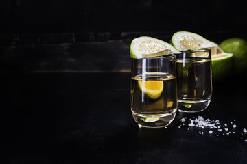 Golden tequila shots with sea salt, juicy lime on vintage black wooden board, toned, selective...