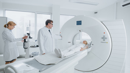In Medical Laboratory Female Radiologist and Male Doctor Control and Monitor MRI or CT Scan with Female Patient Undergoing Procedure. High-Tech Modern Medical Equipment. 