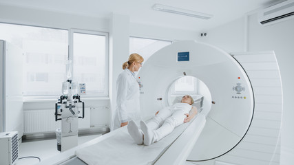 In Medical Laboratory Female Radiologist Controls MRI or CT Scan with Female Patient Undergoing Procedure. High-Tech Modern Medical Equipment.  - obrazy, fototapety, plakaty