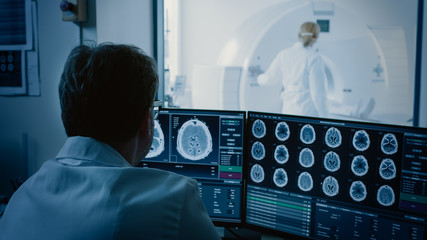 In Medical Laboratory Patient Undergoes MRI or CT Scan Process under Supervision of Radiologist, in Control Room Doctor Watches Procedure and Monitors with Brain Scans Results. - obrazy, fototapety, plakaty