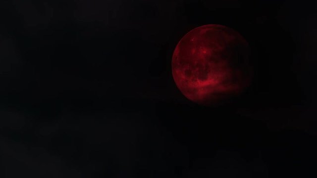 Scary Spooky Blood Red Moon partially obscured by clouds over dark  night sky