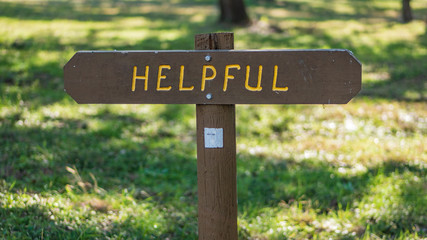Brown wooden sign in grassy field with helpful written on it