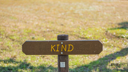 Brown wooden sign in grassy field with kind written on it