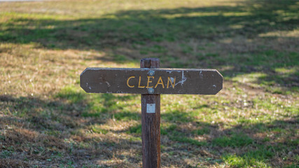 Brown wooden sign in grassy field with clean written on it