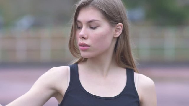 Portrait of a cute girl showing strength. Young girl with dark hair shows biceps at the stadium Beautiful girl in a sports t-shirt showing biceps outdoors Healthy lifestyle