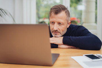 Man leaning on a table reading on his laptop