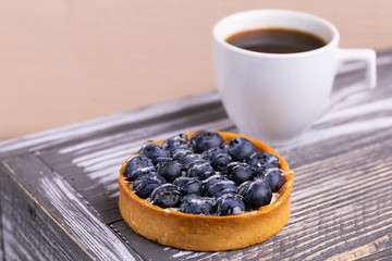 Tasty blueberry tartlet with vanilla cream and cup of coffee