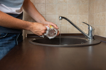 Photo of side of man's hands washing transparent mug in sink