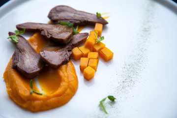 beef tongue cut into pieces with pieces of orange pumpkin lies on a white plate 
