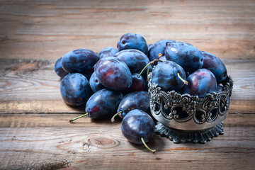 Ripe plums scattered on wooden background.