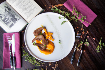 beef tongue cut into pieces with pieces of orange pumpkin lies on a white plate on a dark wooden table with purple cloth napkins