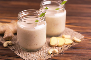 Banana and almond smoothie with ginger in glass jars with paper straws on rustic wooden table....