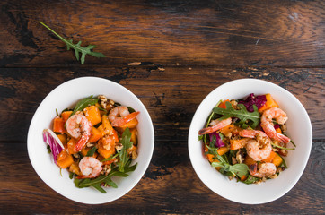 Light fruit salad with fried prawns, persimmon, arugula and walnuts in white bowls on wooden rustic table, top view
