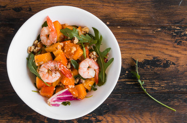 Light fruit salad with fried prawns, persimmon, arugula and walnuts in white bowls on wooden rustic table, top view