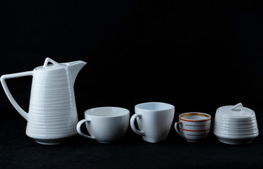 Three cups of different sizes, a teapot for tea and sugar bowl stand on a black background.