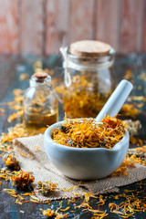 Bottles and dried calendula officinalis petals with macerated oil on wooden background.