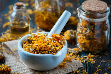 Bottles and dried calendula officinalis petals with macerated oil on wooden background.