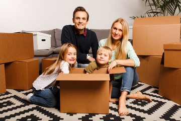 Fototapeta na wymiar Photo of happy parents with children sitting on floor among cardboard boxes