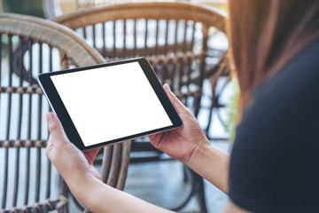 Mockup image of a woman holding and using black tablet pc with blank white desktop screen while sitting in the outdoors