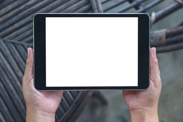 Top view mockup image of hands holding and using black tablet pc with blank white desktop screen while sitting in outdoor