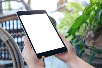 Mockup image of hands holding and using black tablet pc with blank white desktop screen while sitting in the outdoors