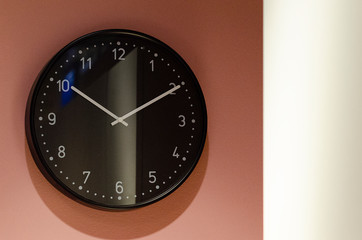 big black clock with white arrows and numbers hang on the pink wall